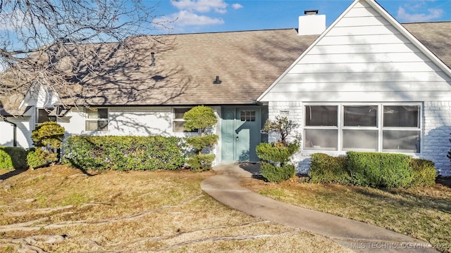 view of front of property with roof with shingles, a front lawn, and a chimney