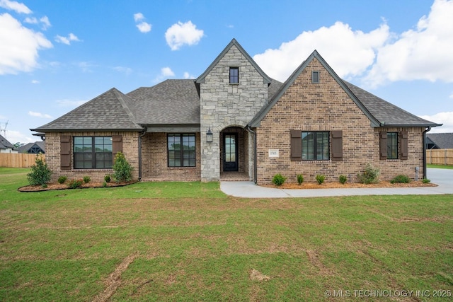 french country inspired facade with brick siding, roof with shingles, fence, and a front yard