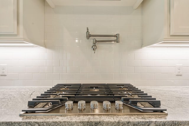 interior details with stainless steel gas stovetop, light stone counters, and decorative backsplash