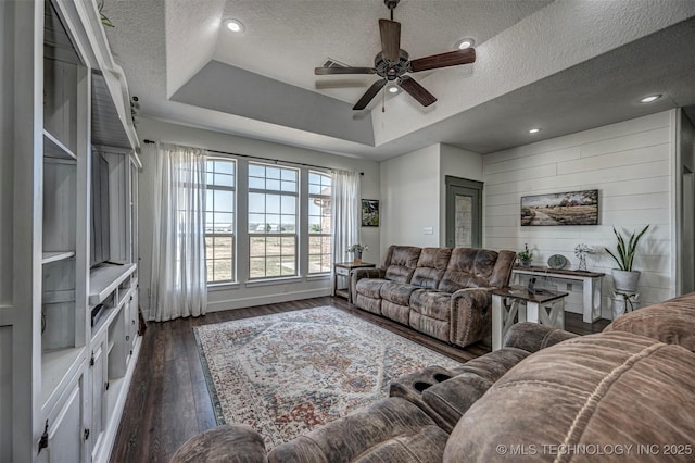 living area with wooden walls, a raised ceiling, a ceiling fan, dark wood-style floors, and a textured ceiling