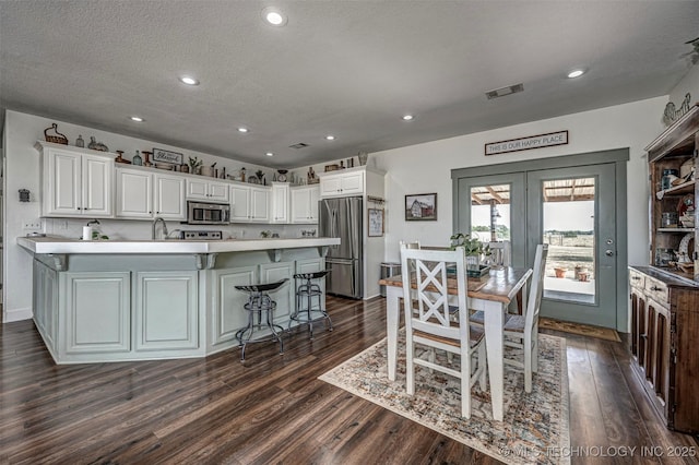 kitchen featuring a textured ceiling, stainless steel appliances, dark wood-type flooring, visible vents, and white cabinets