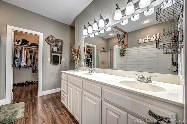 bathroom with double vanity, wood finished floors, a sink, and a shower stall