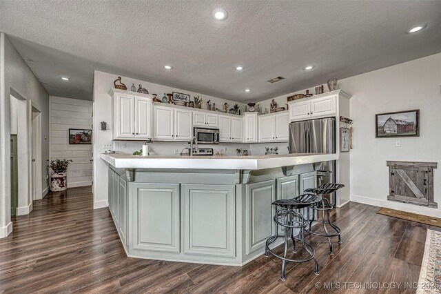 kitchen with white cabinets, stainless steel appliances, dark wood-style flooring, and a kitchen breakfast bar