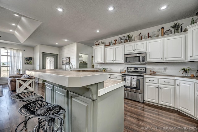 kitchen featuring a center island with sink, dark wood finished floors, stainless steel appliances, a kitchen bar, and white cabinetry