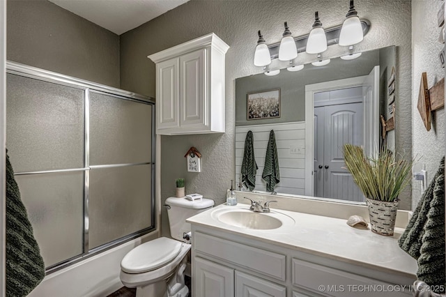 bathroom featuring toilet, vanity, enclosed tub / shower combo, and a textured wall