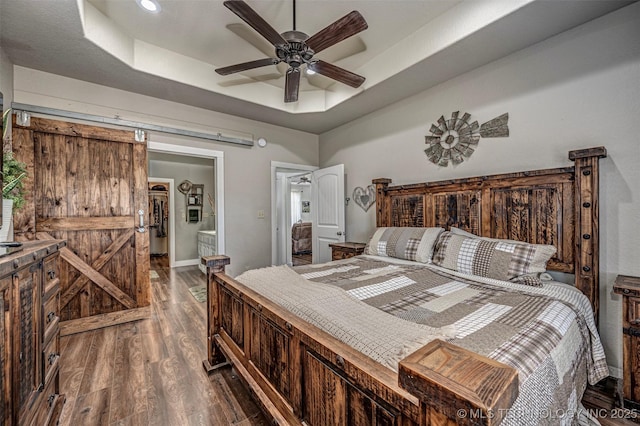 bedroom featuring ceiling fan, a barn door, dark wood finished floors, baseboards, and a raised ceiling