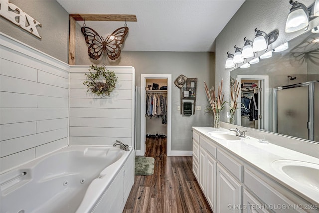 bathroom with a textured wall, a sink, a shower stall, wood finished floors, and a tub with jets