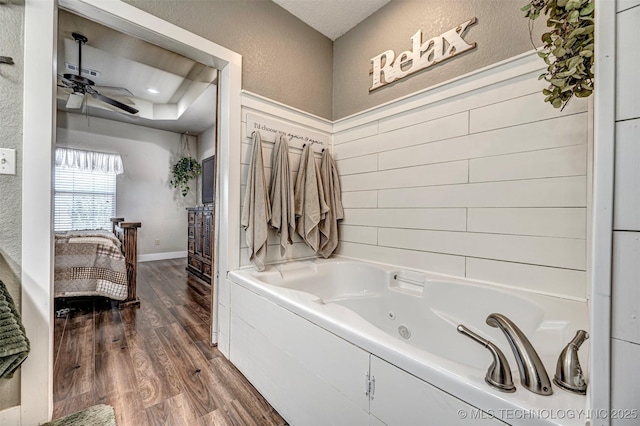 full bathroom featuring baseboards, a textured wall, ceiling fan, a tub with jets, and wood finished floors