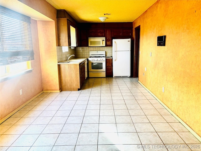 kitchen featuring light tile patterned floors, light countertops, decorative backsplash, a sink, and white appliances