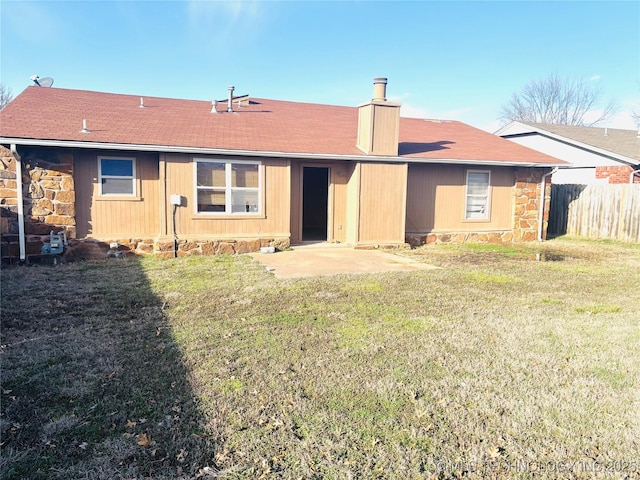 rear view of property with a yard, stone siding, fence, and a chimney