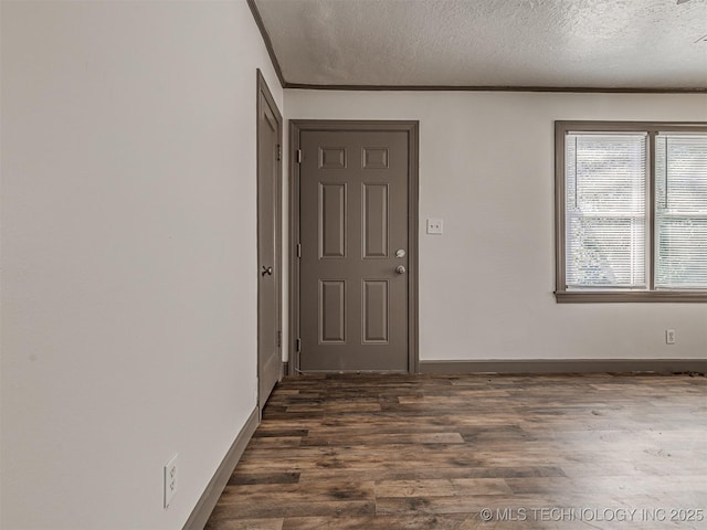 spare room featuring dark wood-style flooring, crown molding, a textured ceiling, and baseboards