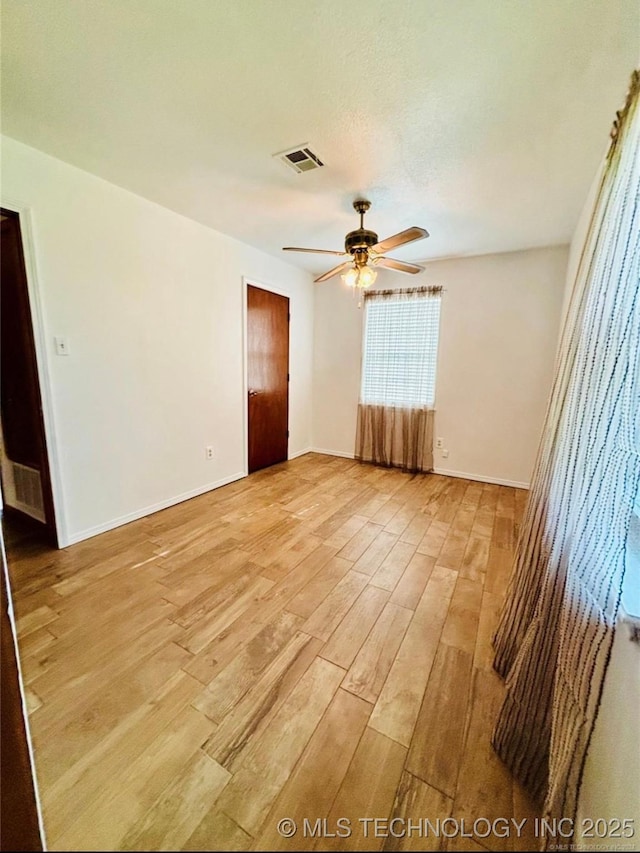 empty room with light wood-type flooring, ceiling fan, visible vents, and baseboards