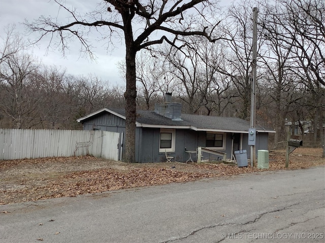 view of front of house with roof with shingles, a chimney, and fence