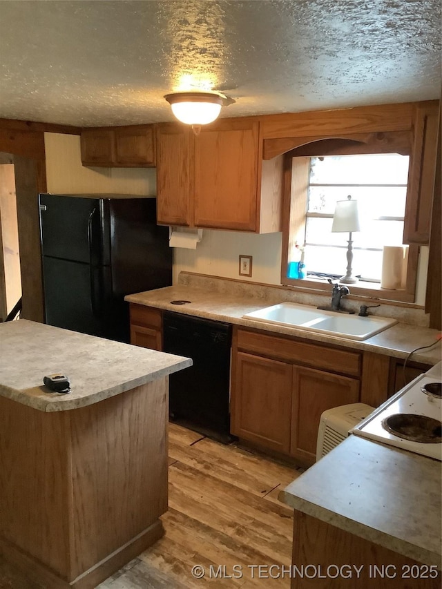 kitchen featuring a textured ceiling, light wood-style flooring, a sink, light countertops, and black appliances