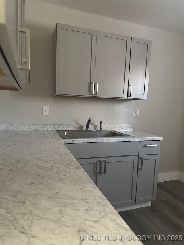 kitchen with gray cabinetry, light countertops, baseboards, and a sink