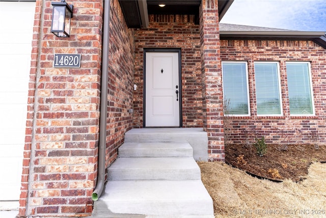 view of exterior entry featuring a garage and brick siding