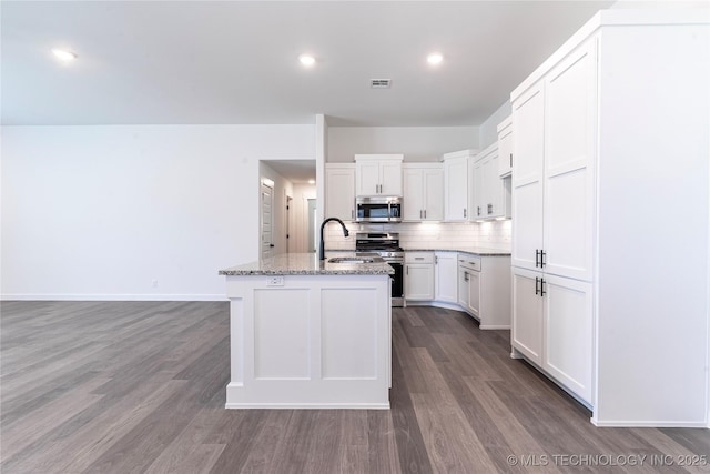 kitchen featuring visible vents, decorative backsplash, light stone counters, appliances with stainless steel finishes, and a sink