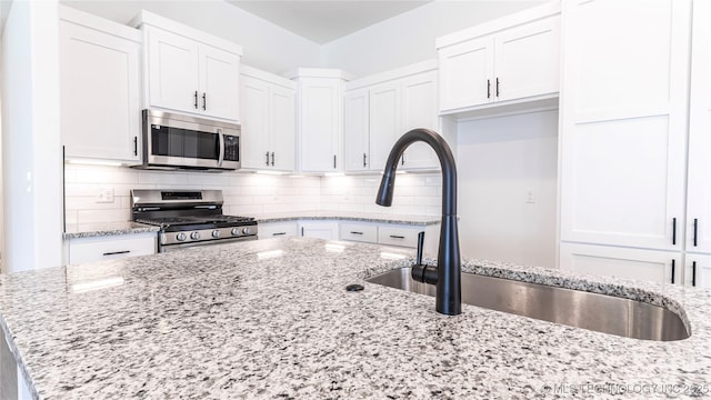 kitchen featuring stainless steel appliances, white cabinets, and backsplash