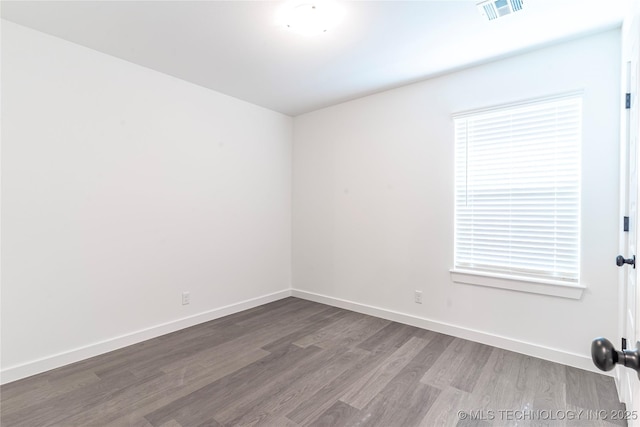 spare room featuring wood finished floors, visible vents, and baseboards