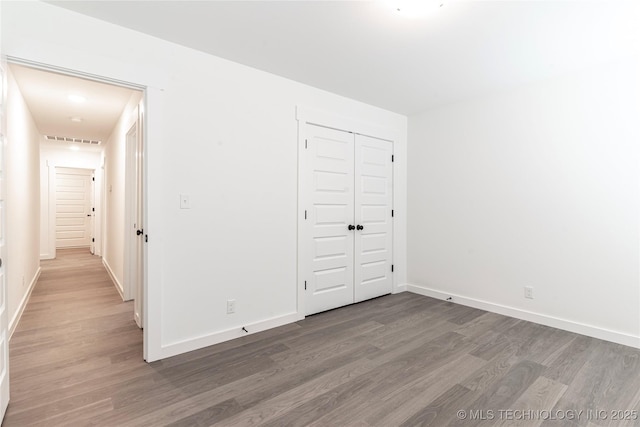 unfurnished bedroom with a closet, wood finished floors, visible vents, and baseboards