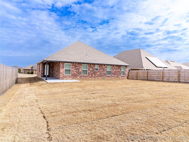 rear view of property featuring brick siding, roof with shingles, a patio area, and a fenced backyard