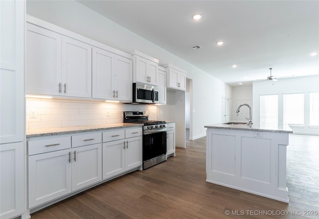 kitchen with white cabinets, appliances with stainless steel finishes, dark wood-style flooring, a sink, and backsplash