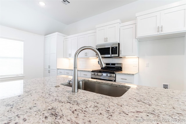 kitchen with a sink, visible vents, white cabinets, appliances with stainless steel finishes, and backsplash