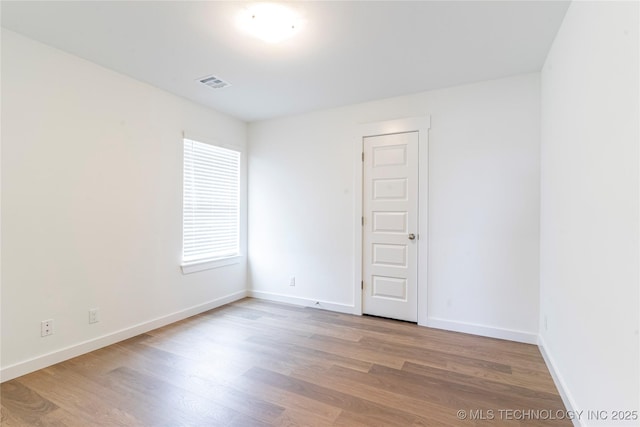 unfurnished room featuring wood finished floors, visible vents, and baseboards