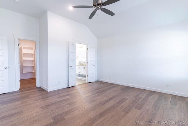 unfurnished bedroom featuring vaulted ceiling, baseboards, a walk in closet, and wood finished floors