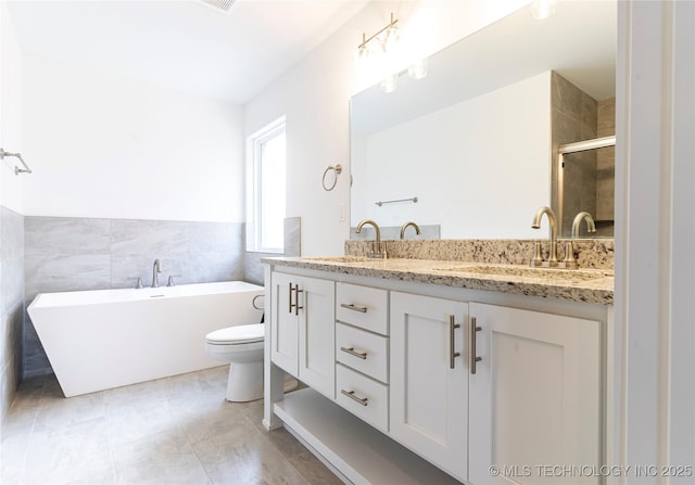 full bathroom with double vanity, a freestanding tub, a sink, and tile walls