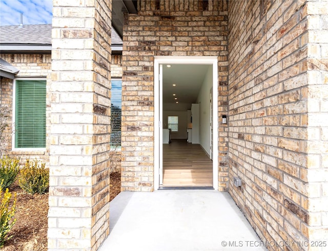 view of exterior entry with stone siding, a shingled roof, and brick siding