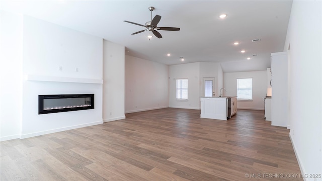 unfurnished living room featuring visible vents, light wood-style flooring, a glass covered fireplace, a sink, and ceiling fan