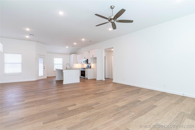 unfurnished living room featuring baseboards, a sink, light wood-style flooring, and a ceiling fan