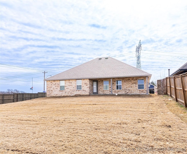 back of house featuring brick siding, a shingled roof, and fence