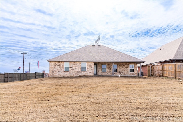 rear view of property featuring brick siding, a shingled roof, and fence