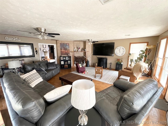 living area with a ceiling fan, a fireplace, and a textured ceiling