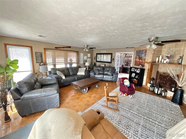 living area featuring visible vents, a ceiling fan, a tile fireplace, wood finished floors, and a textured ceiling