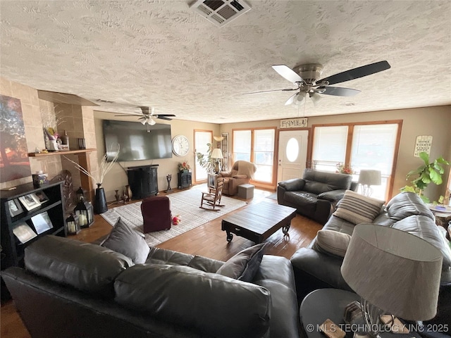 living area featuring a textured ceiling, a large fireplace, wood finished floors, visible vents, and a ceiling fan