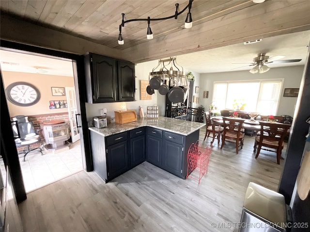 kitchen featuring visible vents, a ceiling fan, a peninsula, light stone countertops, and light wood-style floors