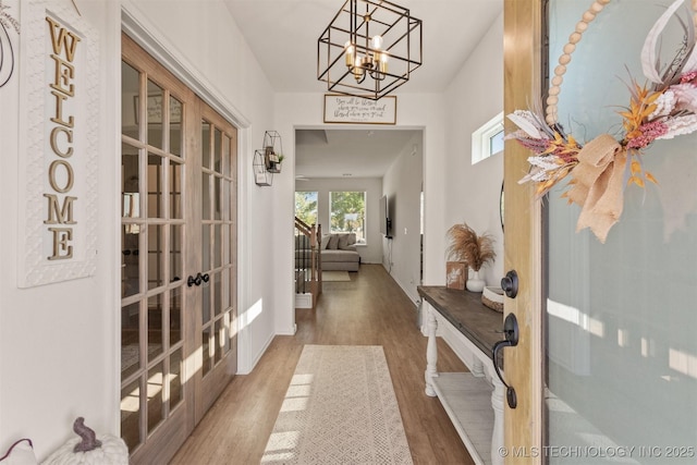 corridor with a notable chandelier, wood finished floors, and french doors