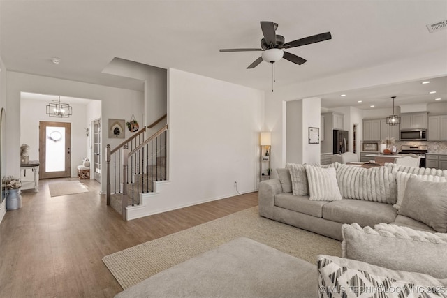 living area featuring recessed lighting, ceiling fan with notable chandelier, wood finished floors, visible vents, and stairs