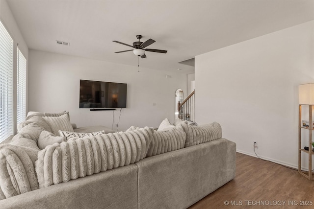 living room featuring baseboards, visible vents, ceiling fan, wood finished floors, and stairs