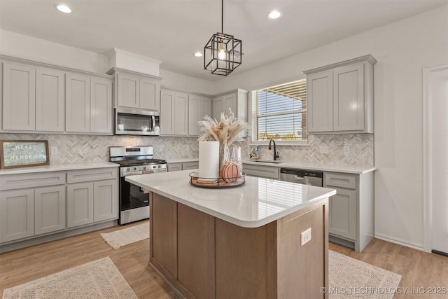 kitchen featuring stainless steel appliances, gray cabinets, light countertops, a sink, and light wood-type flooring