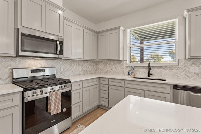 kitchen with tasteful backsplash, light countertops, appliances with stainless steel finishes, a sink, and light wood-type flooring