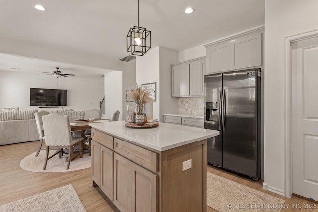 kitchen with a kitchen island, light countertops, light wood-type flooring, backsplash, and stainless steel fridge