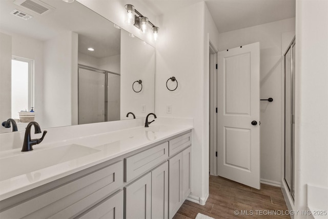 full bath featuring double vanity, a stall shower, a sink, and wood finished floors