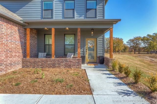 view of exterior entry featuring a porch and brick siding