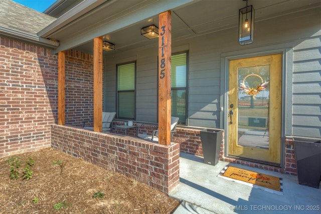 doorway to property featuring a porch, brick siding, and a shingled roof