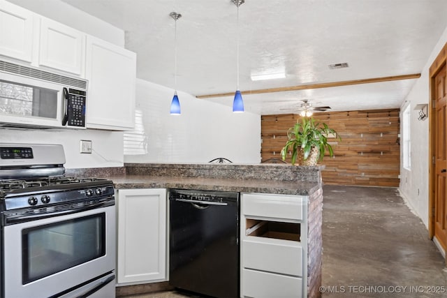 kitchen with stainless steel appliances, dark countertops, visible vents, white cabinetry, and wood walls