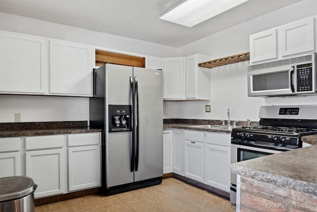 kitchen featuring white cabinets, dark countertops, stainless steel appliances, light floors, and a sink